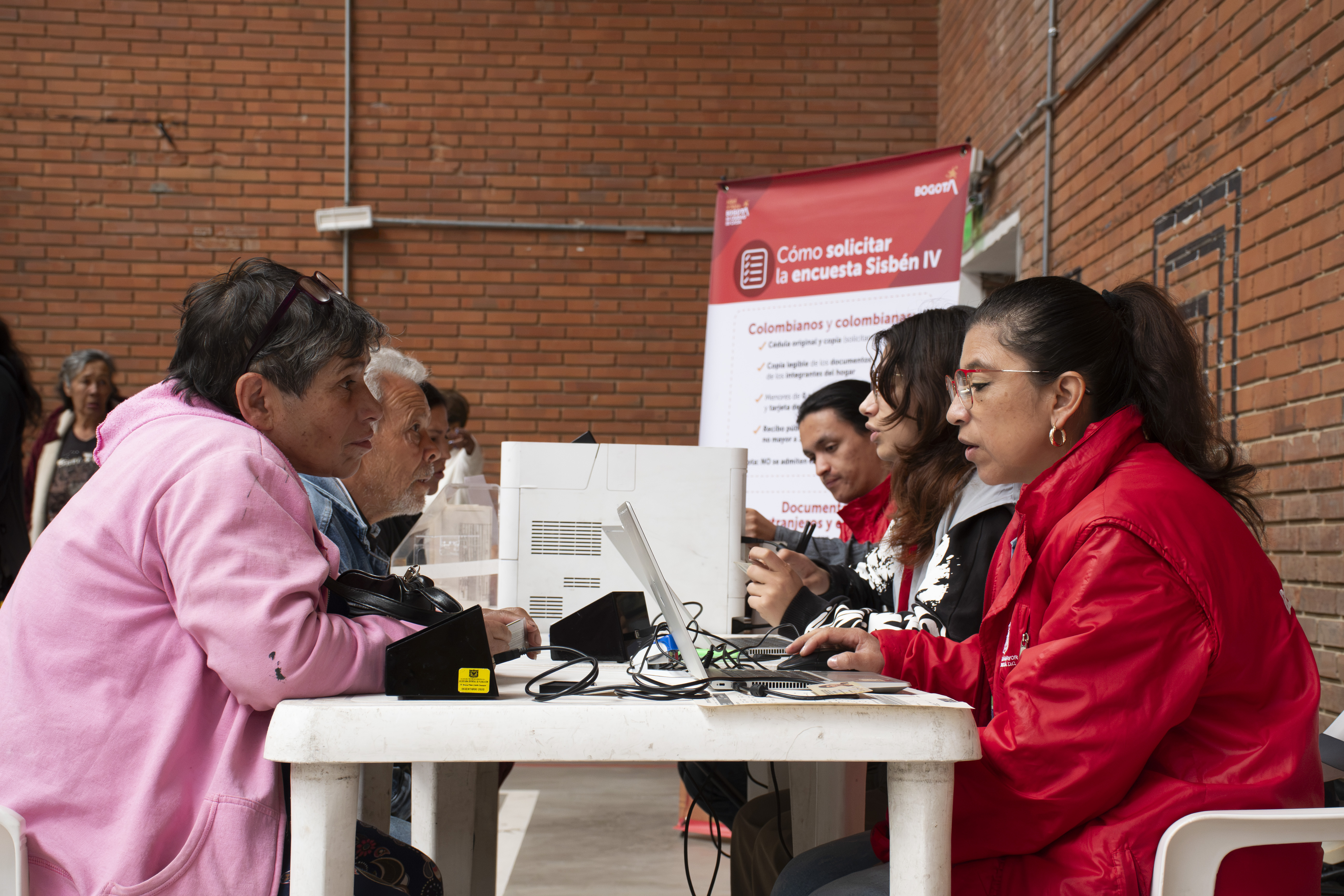 Personas sentadas en una mesa con computadores haciendo trámites