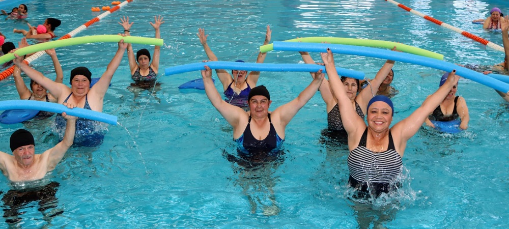 Personas de la tercera edad felices e la piscina levantando los brazos