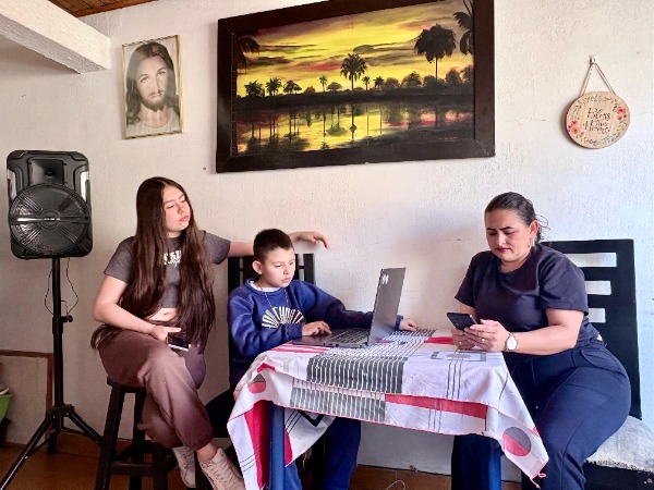 Foto de familia sentada en la sala del hogar  con computador y celular en la mano